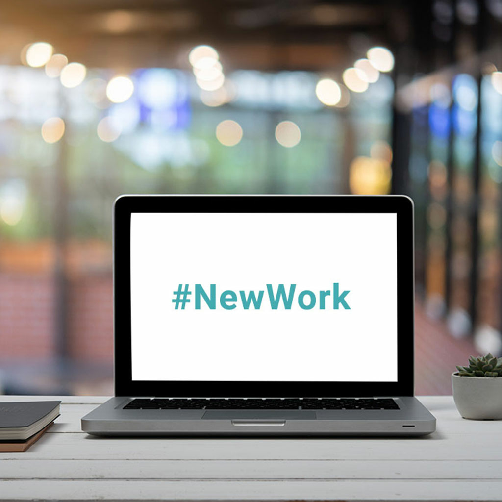Aufgeklappter Monitor auf Schreibtisch mit dem Schriftzug "New Work"